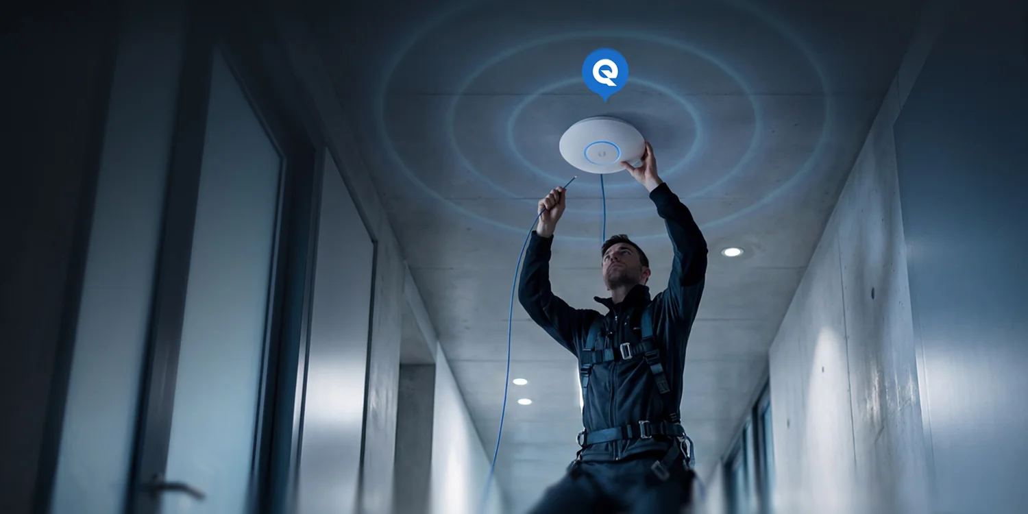 Technician installing a ceiling Wi-Fi access point in a hallway, connecting a cable as blue signal rings spread out