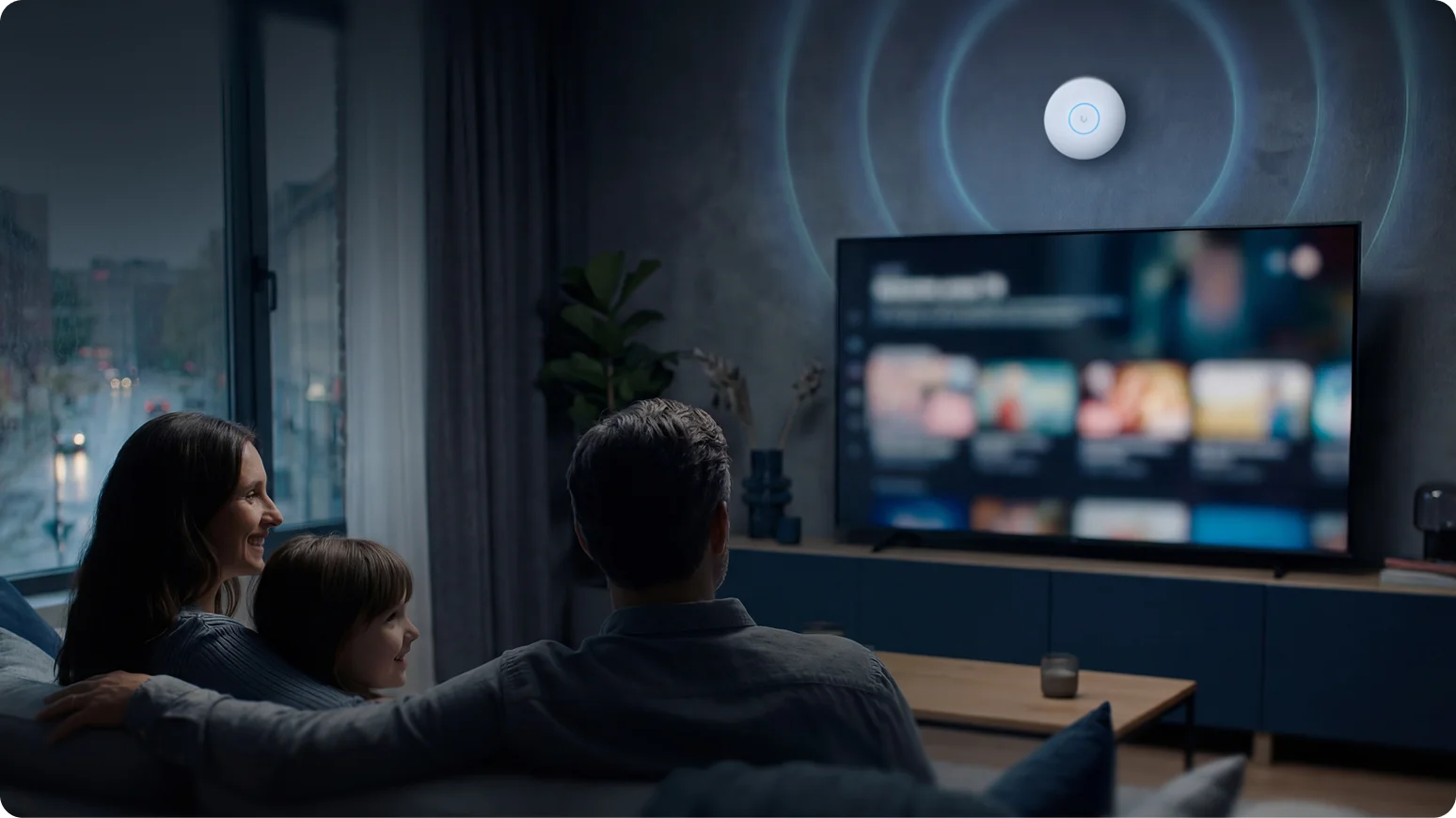 Family on a couch watching a streaming TV at night with a wall-mounted Wi-Fi access point emitting blue signal rings above it